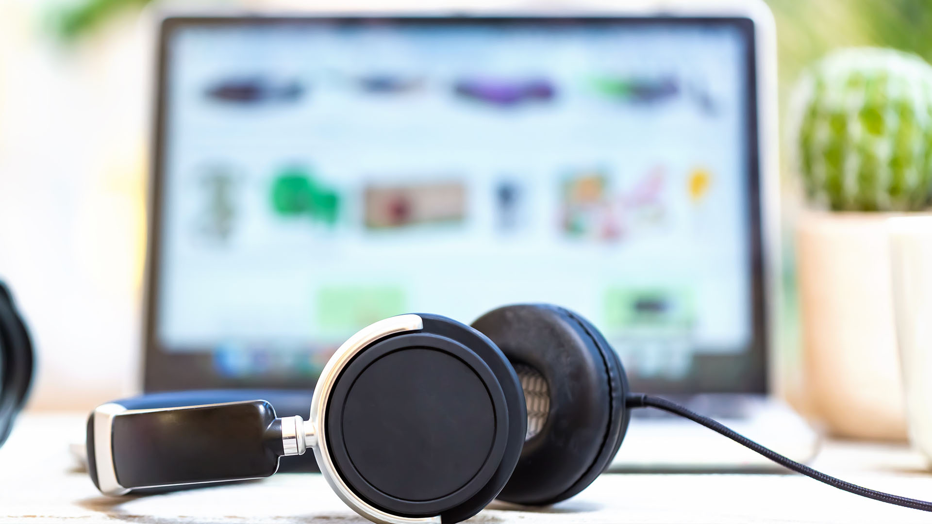 Headphones in the foreground with a laptop screen blurred in the background