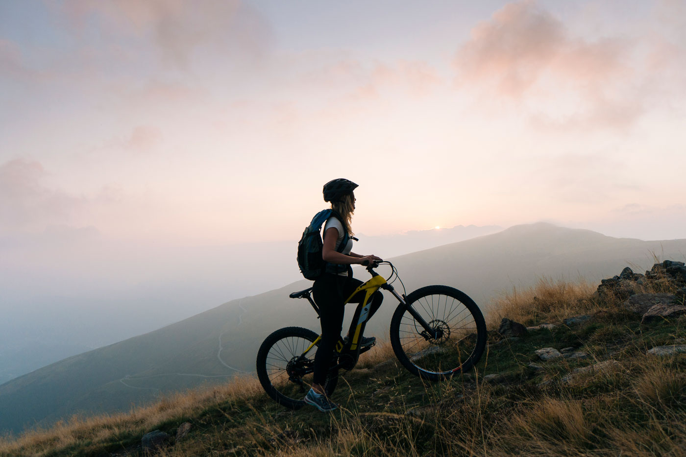 Female mountain biker pauses in alpine track, sunrise